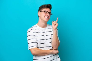 Mavi arka planda izole edilmiş yakışıklı Brezilyalı adam harika bir fikre işaret ediyor.