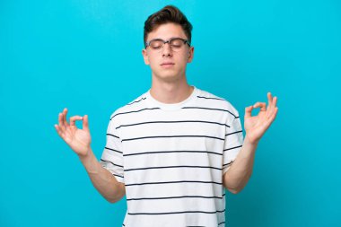 Genç ve yakışıklı Brezilyalı bir adam Zen pozunda mavi arka planda izole edilmiş.