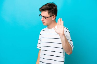 Genç ve yakışıklı Brezilyalı adam mavi arka planda izole edilmiş. Durma hareketi yapıyor ve hayal kırıklığına uğruyor.