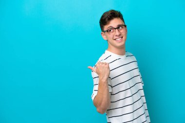 Mavi arka planda izole edilmiş yakışıklı Brezilyalı genç bir adam bir ürün sunmak için kenarı işaret ediyor.