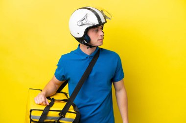 Sırt çantalı genç Brezilyalı adam, sarı arka planda izole edilmiş, yana bakıyor.