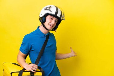 Sırt çantalı genç Brezilyalı adam sarı arka planda izole edilmiş. Davet etmek için ellerini yana uzatıyor.