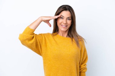 Beyaz arka planda izole edilmiş orta yaşlı beyaz kadın mutlu bir ifadeyle selam veriyor.