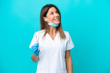 Orta yaşlı doktor kadın mavi arka planda izole edilmiş bir şekilde bakarken bir fikir düşünüyor.