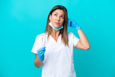 Mavi arka planda izole edilmiş orta yaşlı doktor kadının şüpheleri ve düşünceleri var.