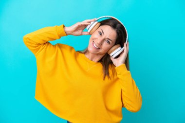 Orta yaşlı beyaz kadın mavi arka planda izole edilmiş müzik dinliyor.