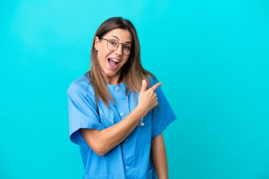 Mavi arka planda izole edilmiş orta yaşlı cerrah kadın şaşırmış ve işaret ediyor.