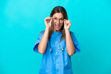 Mavi arka planda gözlüklü ve şaşırmış orta yaşlı cerrah kadın.