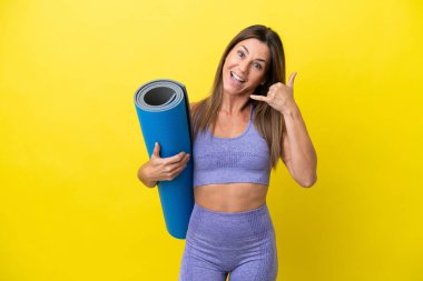 Elinde minder tutarken yoga derslerine giden sporcu bir kadın telefon hareketleriyle izole edilmiş sarı olmayan bir arka plan. Bana geri dönüş işareti ver.