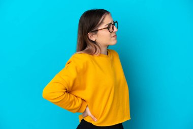 Genç, beyaz bir kadın, mavi arka planda izole edilmiş. Çaba gösterdiği için sırt ağrısı çekiyor.