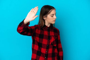 Mavi arka planda izole edilmiş genç beyaz kadın dur hareketi yapıyor ve hayal kırıklığına uğruyor.