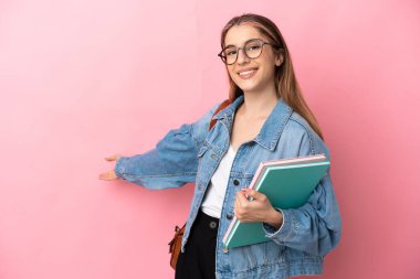 Pembe arka planda izole edilmiş genç beyaz kadın davet edildiği için ellerini yana uzatıyor.