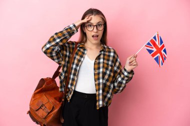 Young hispanic woman holding an United Kingdom flag isolated on pink background with surprise expression