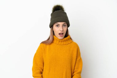 Kışlık şapkalı genç kız, beyaz arka planda, şaşırmış yüz ifadesi ile izole edilmiş.