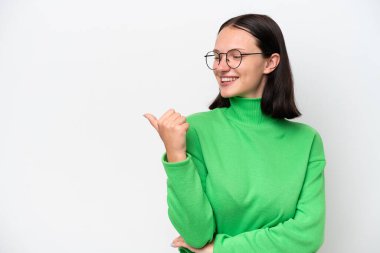 Beyaz arka planda izole edilmiş genç beyaz kadın bir ürünü sunmak için kenarı işaret ediyor.