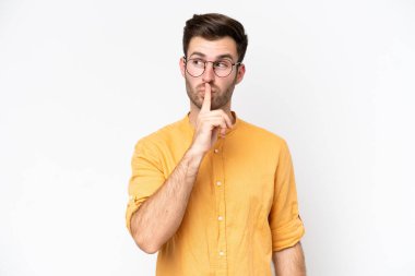 Beyaz arka planda izole edilmiş genç beyaz bir adam sessizlik işareti gösteriyor. Parmağını ağzına sokuyor.