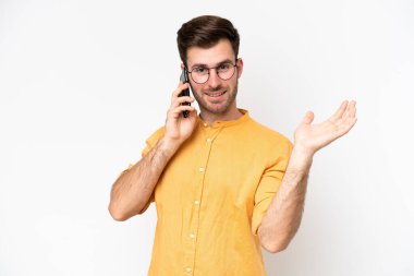 Beyaz arka planda izole edilmiş genç beyaz bir adam cep telefonuyla sohbet ediyor.