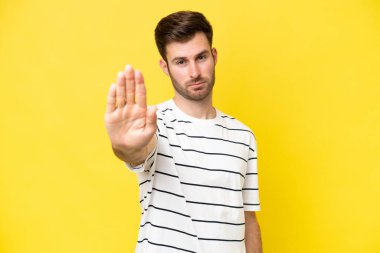 Sarı arka planda izole edilmiş genç beyaz adam dur hareketi yapıyor.