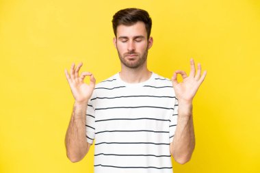 Zen pozisyonunda sarı arka planda izole edilmiş genç beyaz adam.