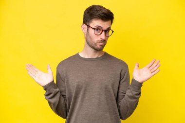 Sarı arka planda izole edilmiş genç beyaz adam şüpheli hareketler yapıyor.