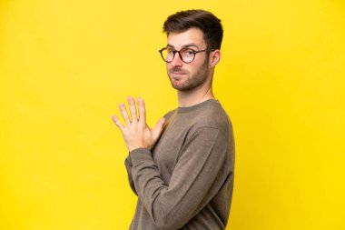 Genç beyaz adam sarı arka planda izole edilmiş bir şeyler çeviriyor.