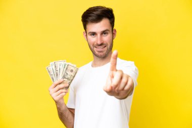Genç beyaz adam, sarı arka planda izole edilmiş bir şekilde çok para alıyor.