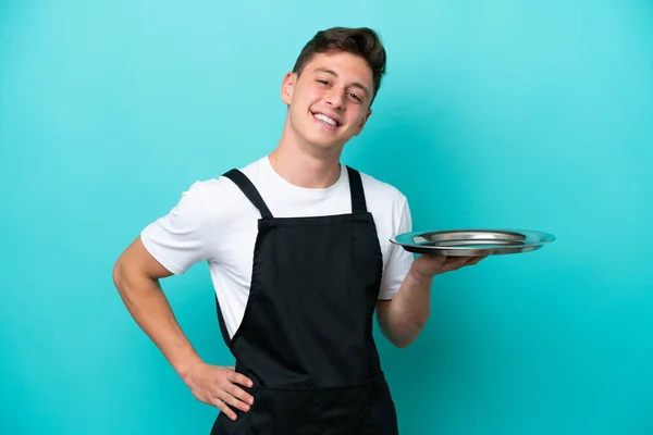 Young Waitress Tray Isolated Blue Background Posing Arms Hip Smiling — Φωτογραφία Αρχείου