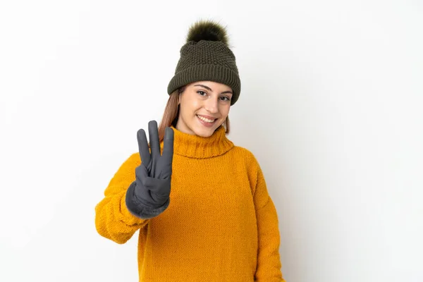年轻姑娘戴着冬帽 背景洁白 心情愉快 用手指数着三个 — 图库照片