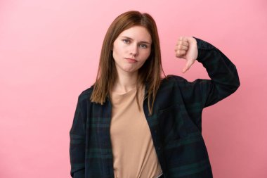 Pembe arka planda izole edilmiş genç bir İngiliz kadın, olumsuz ifadeyle baş parmağını aşağı gösteriyor.