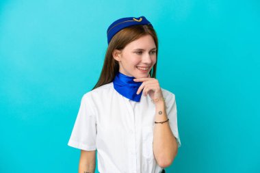 Uçak hostesi İngiliz kadın mavi arka planda izole edilmiş, yan tarafa bakıyor.