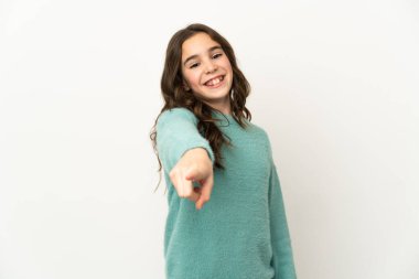 Beyaz arka planda izole edilmiş küçük beyaz kız mutlu bir ifadeyle ön tarafı işaret ediyor.