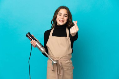 Mavi arka planda el blenderi kullanan küçük bir kız para hareketi yapıyor.