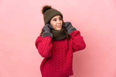 Pembe arka planda izole edilmiş küçük bir kız hayal kırıklığına uğramış ve kulaklarını kapatmış.