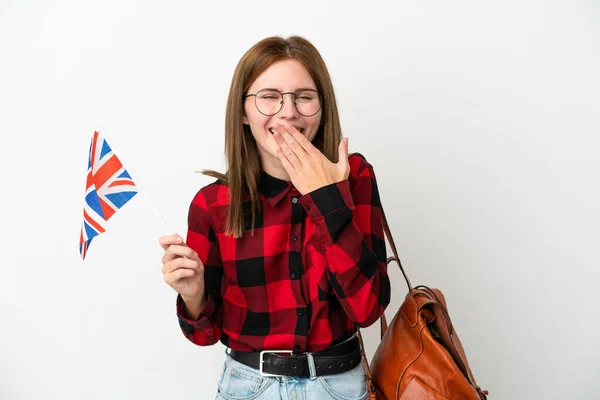 Young woman holding an United Kingdom flag isolated on blue background happy and smiling covering mouth with hand