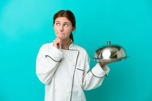 Young chef woman with tray isolated on blue background having doubts and thinking