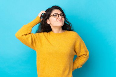 Teenager Russian girl isolated on blue background having doubts while scratching head