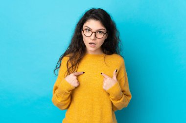 Teenager Russian girl isolated on blue background pointing to oneself