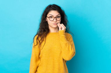 Teenager Russian girl isolated on blue background showing a sign of silence gesture