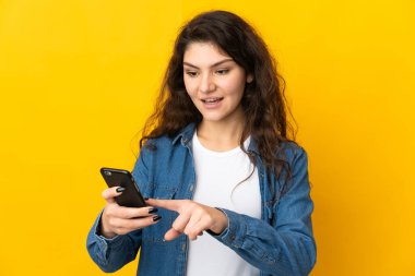 Genç Rus kız sarı arka planda izole edilmiş cep telefonuyla mesaj ya da e-posta gönderiyor.