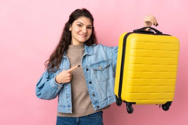 Young woman over isolated pink background in vacation with travel suitcase