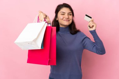 Pembe arka planda izole edilmiş genç bir Rus kız elinde alışveriş çantaları ve bir kredi kartı tutuyor.