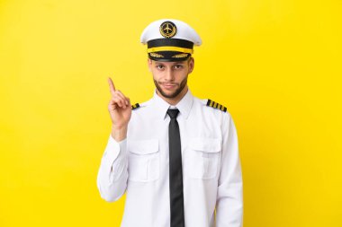 Kafkasyalı uçak pilotu sarı arka planda izole edilmiş işaret parmağıyla işaret etmek harika bir fikir.