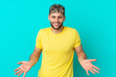 Mavi arka planda izole edilmiş yakışıklı beyaz adam mutlu ve gülümsüyor.