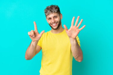 Mavi arka planda izole edilmiş yakışıklı beyaz adam yediyi parmaklarıyla sayıyor.