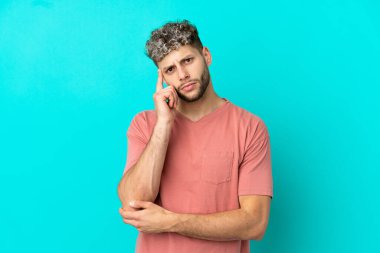 Genç, yakışıklı, beyaz bir adam mavi arka planda izole edilmiş bir fikir düşünüyor.