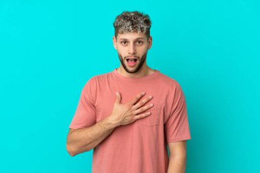 Mavi arka planda izole edilmiş yakışıklı beyaz adam sağa bakarken şaşırdı ve şok oldu.