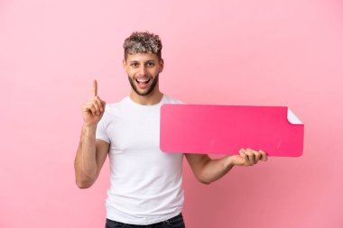 Pembe arka planda izole edilmiş yakışıklı beyaz bir adam elinde boş bir levha tutuyor.