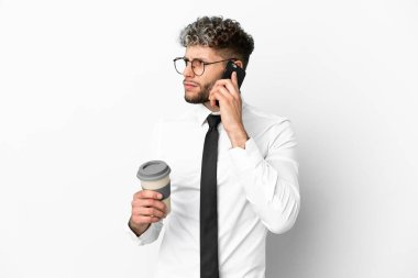 Beyaz arka planda izole edilmiş beyaz bir iş adamı elinde kahve ve bir cep telefonu tutuyor.