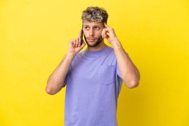Sarı arka planda izole edilmiş cep telefonu kullanan beyaz bir genç şüpheleri ve düşünceleri var.