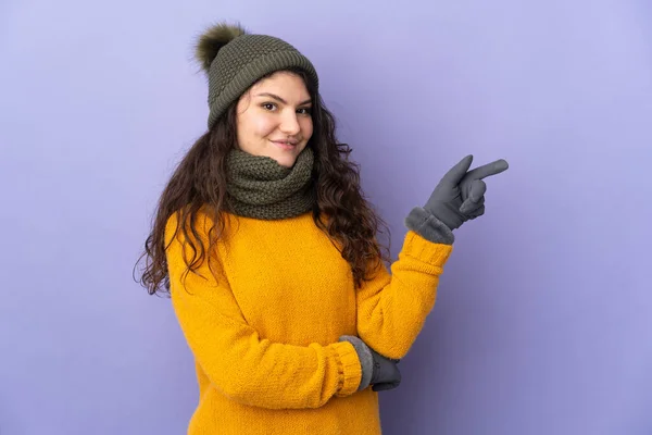 俄罗斯少女 头戴紫色背景的冬帽 手指指向侧面 — 图库照片